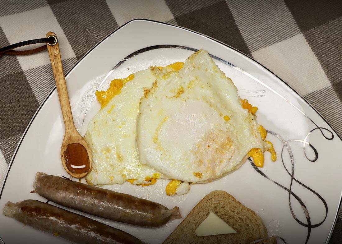 Cooked Egg Basket eggs on a plate with sausage, toast, and honey