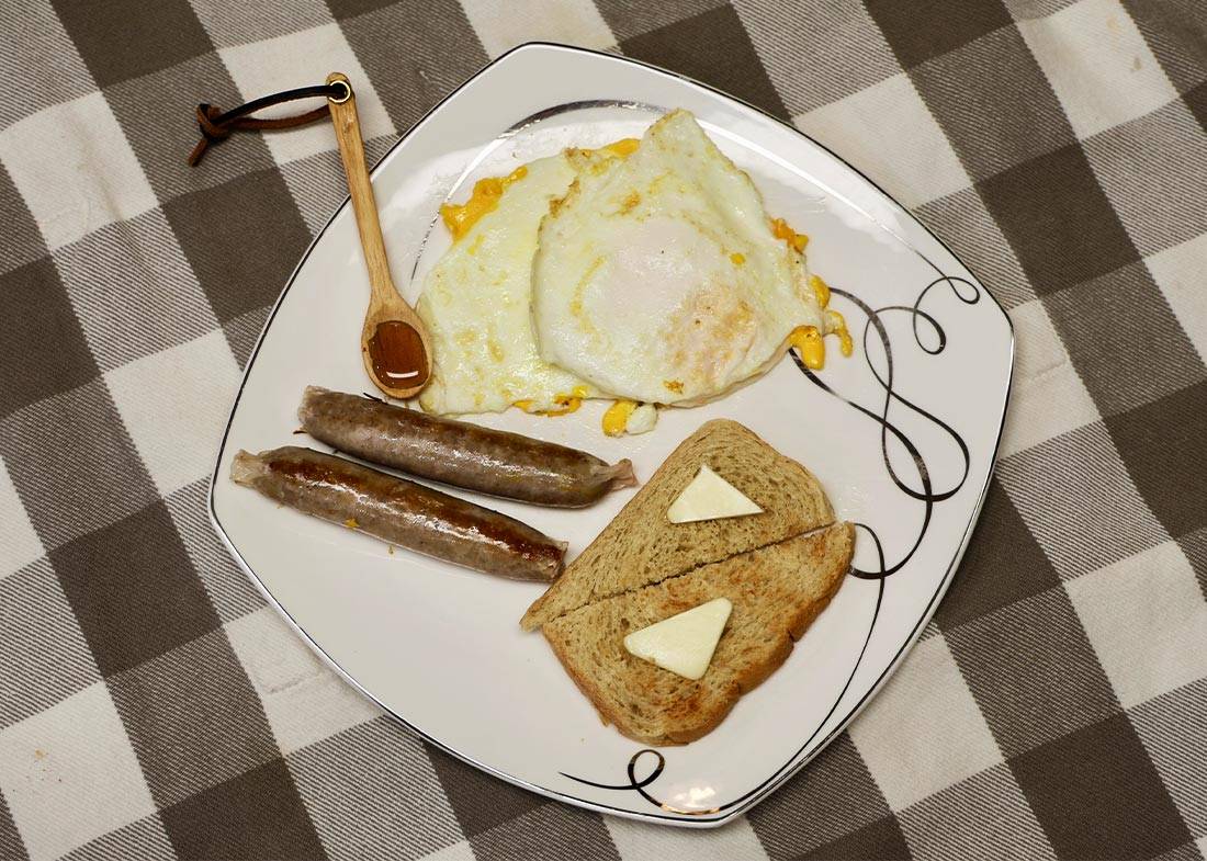 Cooked Egg Basket eggs on a plate with sausage, toast, and honey