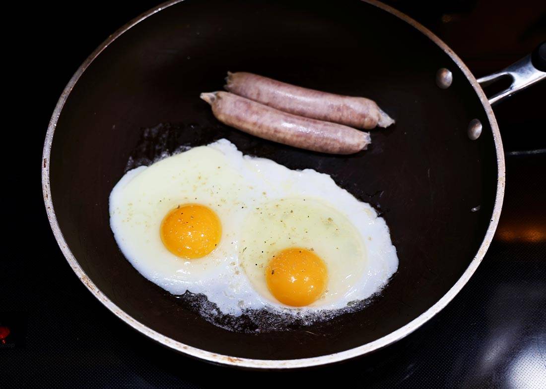 The Egg Basket eggs being cooked in pan with two sausage links